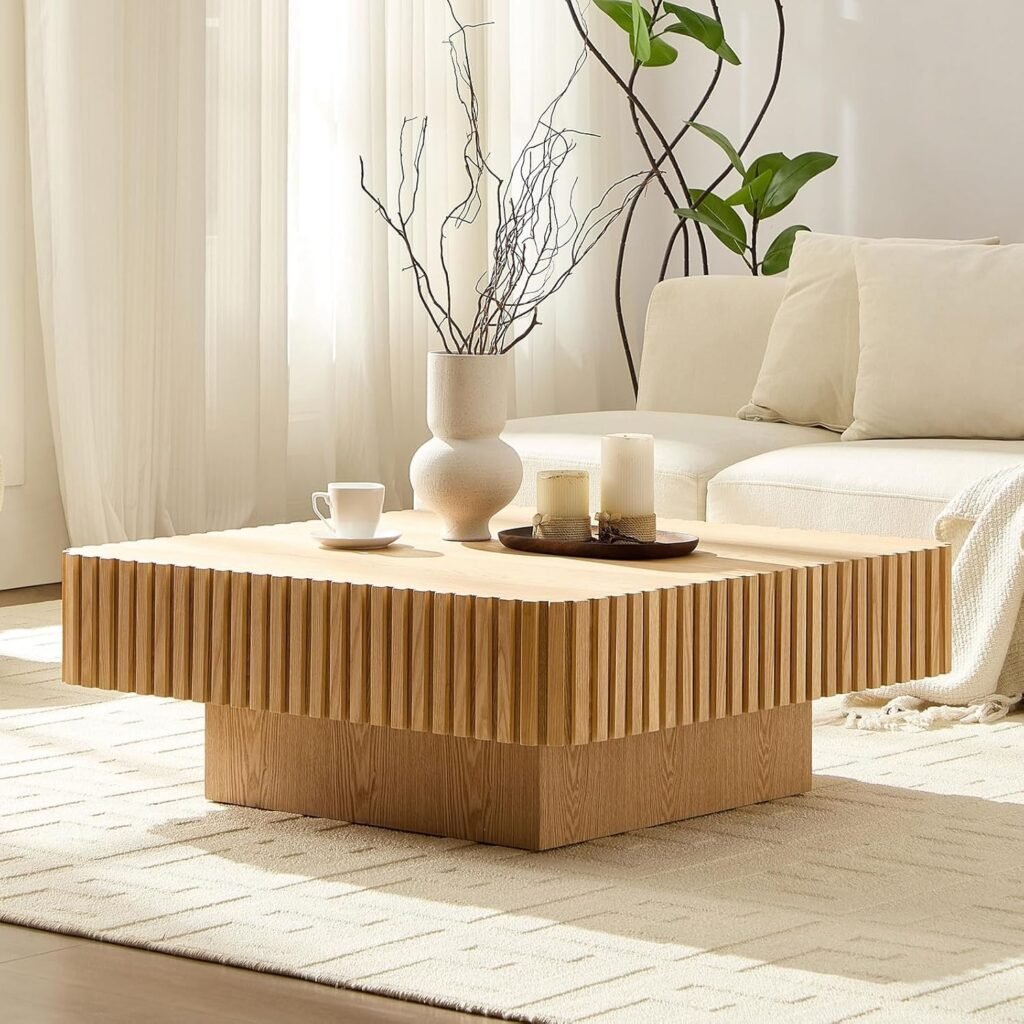 Square Japandi coffee table with fluted wooden detailing and pedestal base, styled with candles and a ceramic vase in a light-filled room.