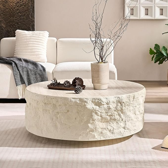Round coffee table with a textured stone-look base and smooth wood top styled in a neutral Organic Modern living room.