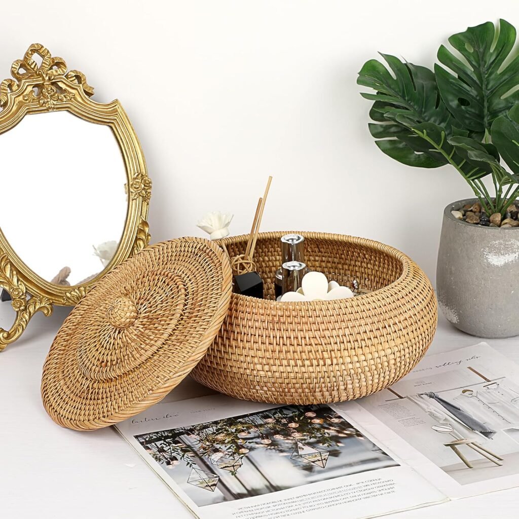 Round woven rattan storage basket with lid styled on a tabletop beside a mirror and greenery.