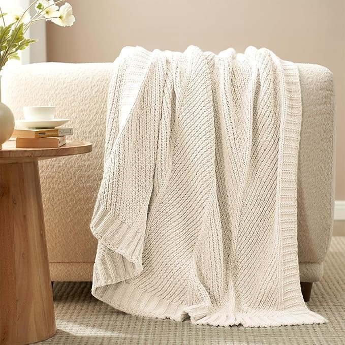 Soft ivory knit throw blanket draped over a cozy chair in a neutral Japandi-inspired living room.