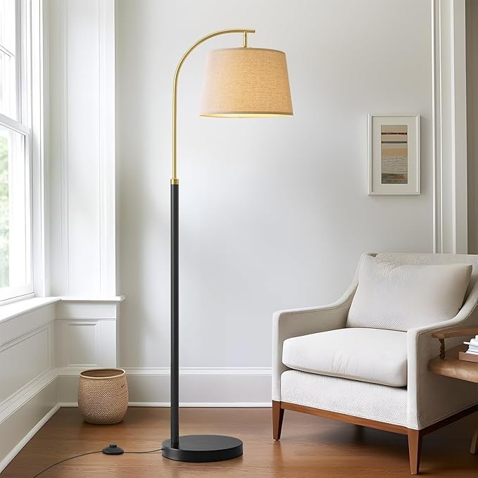 Japandi-inspired modern floor lamp with curved black base and linen shade next to a neutral armchair.