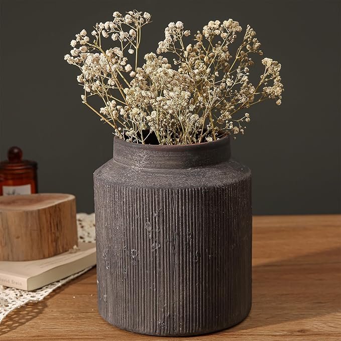 Dark textured ceramic vase filled with dried baby’s breath flowers on a wooden table.