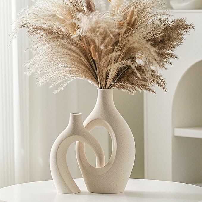 Modern set of two cream-colored vases with open, sculptural shapes, one filled with pampas grass.