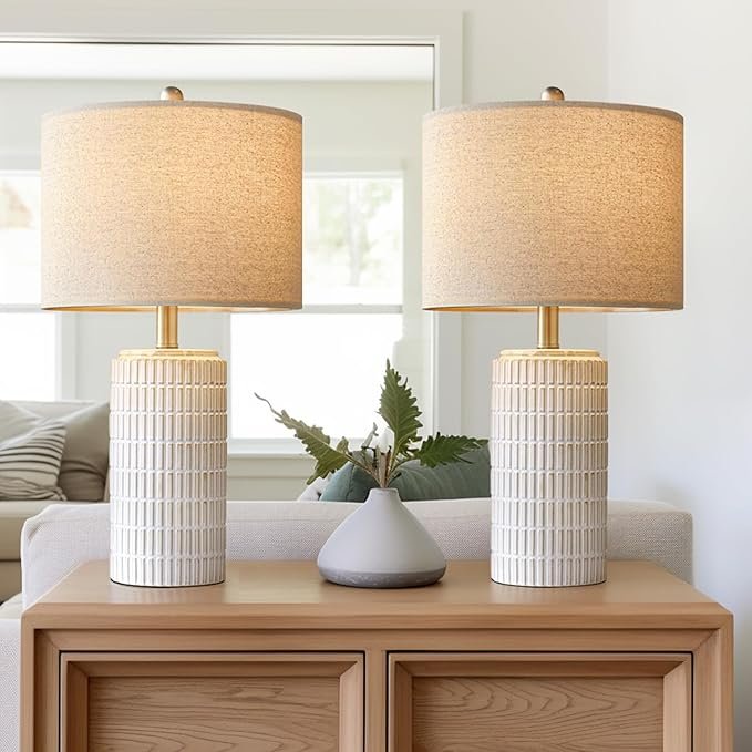 Pair of modern table lamps with textured ceramic bases and linen shades styled on a light wood cabinet in a Japandi-inspired living room.