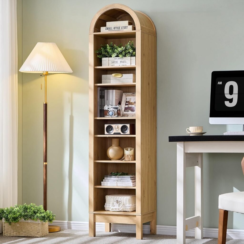 tall arched wooden bookshelf with open shelves styled with books and decor in small home office