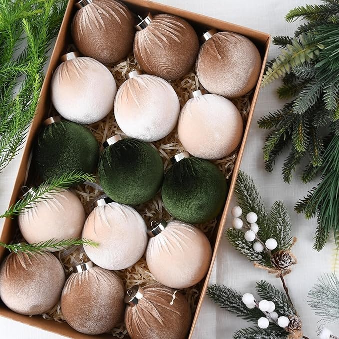 Box of velvet Christmas ornaments in earthy tones of green, bronze, and champagne arranged in holiday greenery.