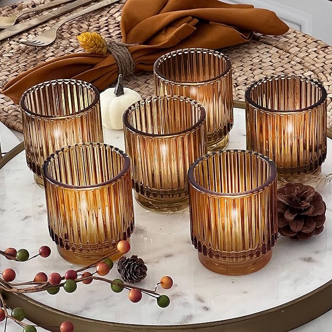 Six ribbed amber glass candle holders glowing with warm candlelight on a fall-inspired table setting.