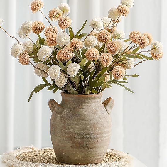 Rustic clay vase filled with neutral beige and white faux flowers, styled on a woven placemat for cozy fall décor.