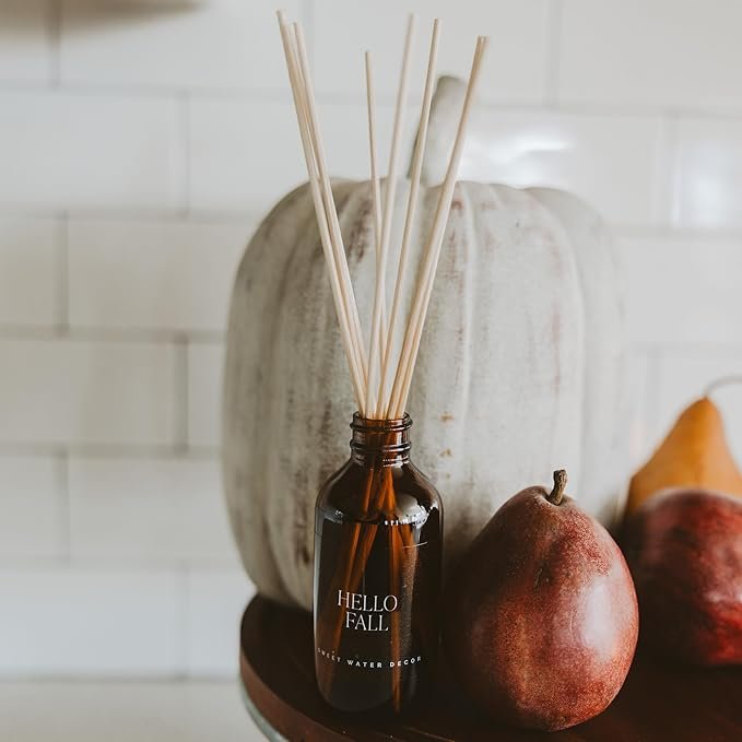 Amber glass reed diffuser bottle with ‘Hello Fall’ label, styled with white pumpkin and pears for seasonal home fragrance décor