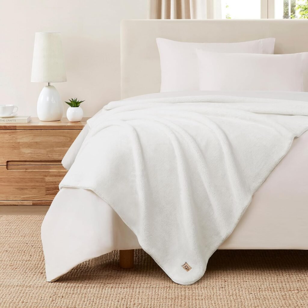 Ultra-soft white throw blanket draped across a neutral bed with wood nightstand and lamp.