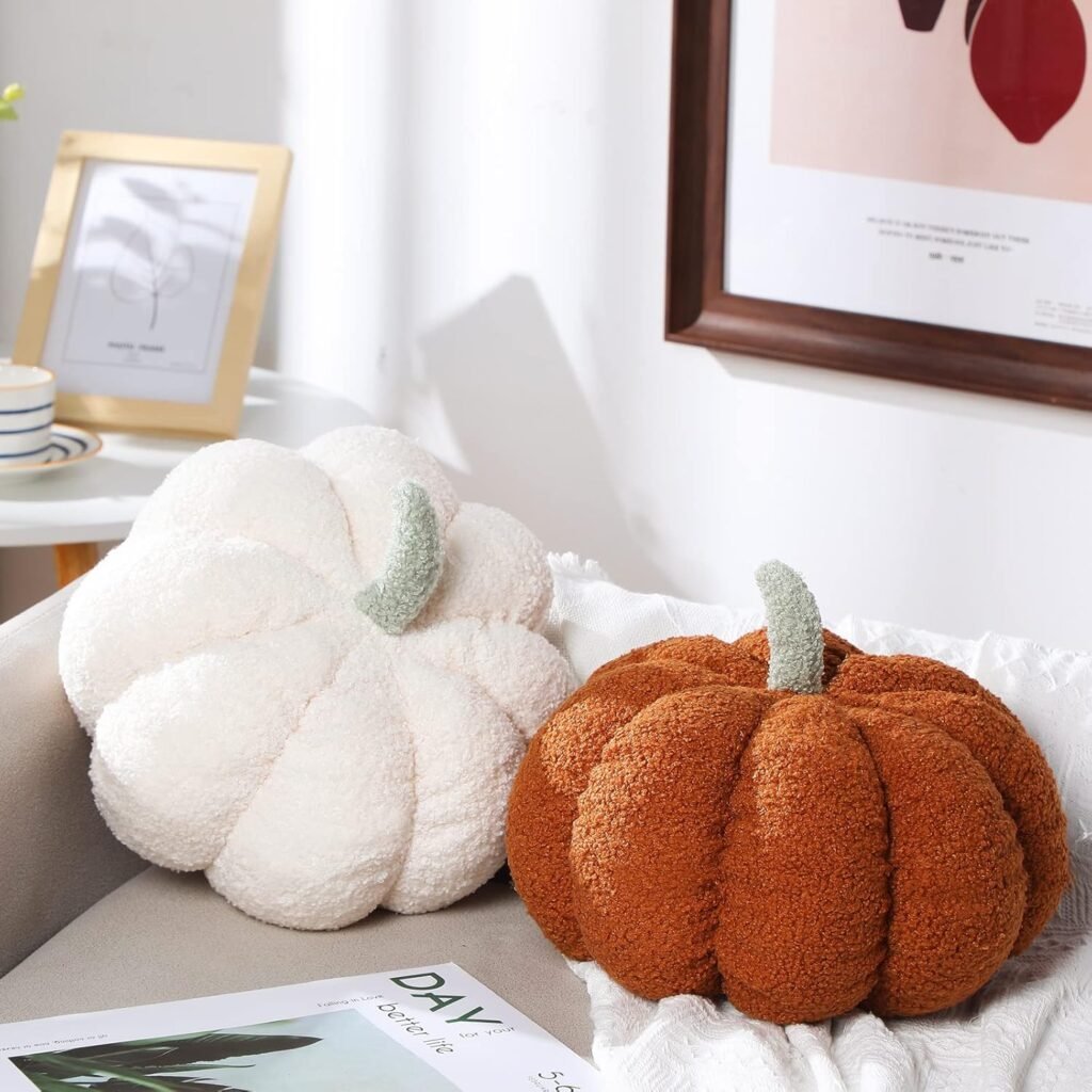 Two plush pumpkin decorations, one in cream and one in burnt orange, styled on a sofa with cozy fall accents.