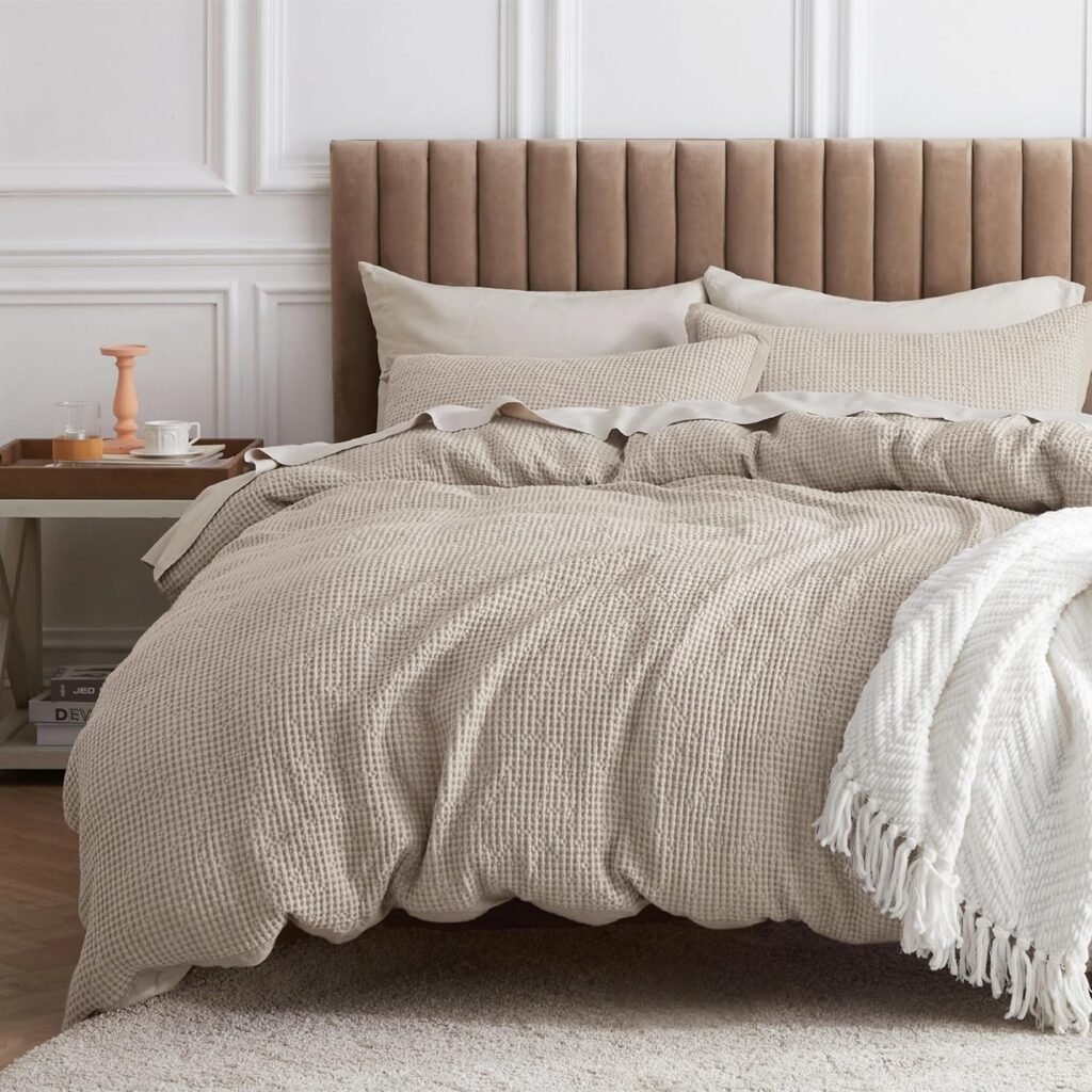 neutral textured bedding set with beige duvet, layered pillows, and white knit throw in a minimalist bedroom